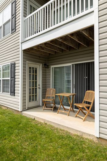 A wooden table and two chairs are on a porch.